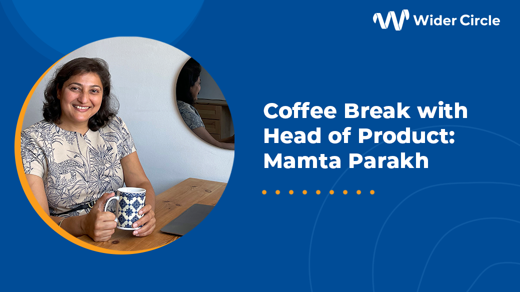 Mamta Employee Spotlight Graphic Photo of Mamta Parakh, Head of Product, Wider Circle, holding a cup of coffee and sitting at her desk